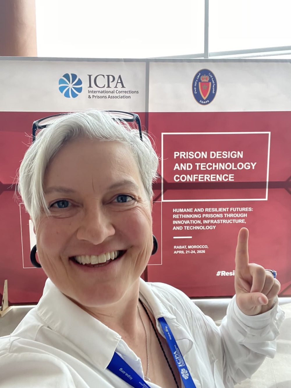 Cathryn Lokey pointing at the banner of the ICPA Prison Design and Technology Conference in Rabat, Morocco